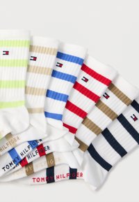 Έξι ζευγάρια λευκές κάλτσες πλήρους μήκους με οριζόντιες ρίγες σε πράσινο, μπεζ, μπλε, κόκκινο, καφέ και μαύρο, κάθε μία με μικρό λογότυπο σημαίας και όνομα μάρκας.