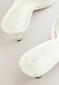 Sandales blanches à talons fins avec semelles intérieures rembourrées, de la marque « NEXT », vues de dessus sur un fond neutre.