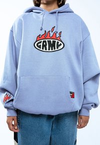 Sudadera morada con un gran logo impreso en llamas que dice "GAMY" en el pecho, con un bolsillo frontal y gráficos de llamas en las mangas.