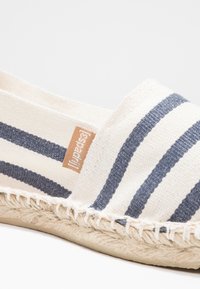 Leinensandale mit horizontalen Streifen in Marineblau und Creme, Juteschnursohle und einem kleinen Markenetikett, das an der Oberseite angebracht ist.