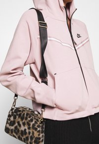 Felpa rosa con zip frontale e dettagli neri, abbinata a una borsa leopardata con tracolla nera e accessori dorati.