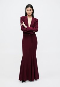 Bordeauxrotes, figurbetontes Kleid mit ausgestelltem Rock, strukturierter Blazer-ähnlicher Oberteil, tiefem V-Ausschnitt und langen Ärmeln. Glatter Stoff mit minimalen Verzierungen.
