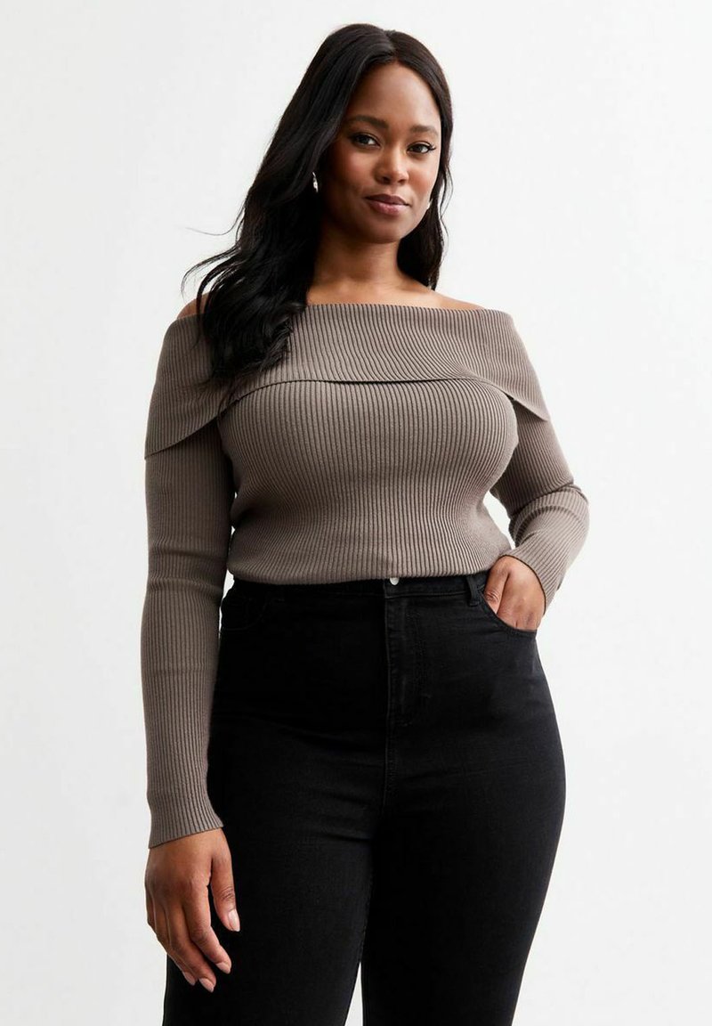 Maglione a spalle scoperte in rib con maniche lunghe, di colore taupe, caratterizzato da un motivo testurizzato. Abbinato a jeans neri a vita alta.