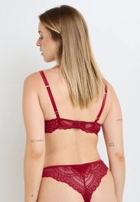 Ensemble soutien-gorge et string en dentelle bordeaux avec motifs floraux complexes, bretelles réglables et bordure festonnée pour une finition élégante.