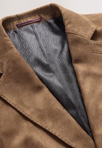 Barna szarvasbőr blézer kis bevágású hajtókákkal, sima szürke mintás béléssel. Varrás részletek a széleken.