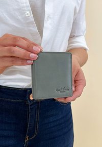 Sivi kožni novčanik držan u ruci, s glatkom teksturom, zaobljenim kutovima, detaljima šivanja i utisnutim logotipom sprijeda.