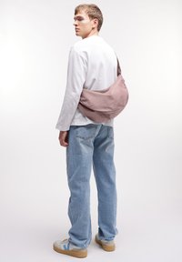 Borsa a spalla grande di tessuto rosa indossata sopra una maglietta bianca a maniche lunghe, abbinata a jeans in denim blu chiaro e sneakers grigie.