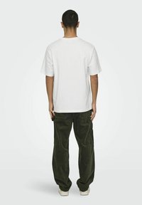 Weißes Baumwoll-T-Shirt mit kurzen Ärmeln, kombiniert mit dunkelgrünen Cordhosen. Das Outfit hat eine lässige Passform und ein einfaches Design.