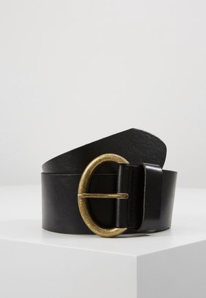 Zwarte leren riem opgerold op een witte ondergrond met een grote antieke goudkleurige metalen D-vormige gesp.