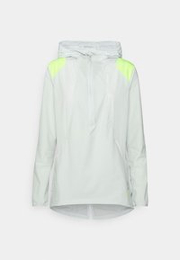 Veste à capuche légère en tissu blanc doux, avec des accents vert fluo sur les épaules, devant zippé à mi-longueur et un dos plus long.