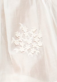 Tissu blanc avec un groupe brodé de petites fleurs blanches et de feuilles en motif circulaire.