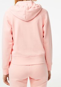 Rosa huva med en slät textur, ribbad mudd och nederkant, med en avslappnad passform och en enkel design utan synliga logotyper eller mönster.