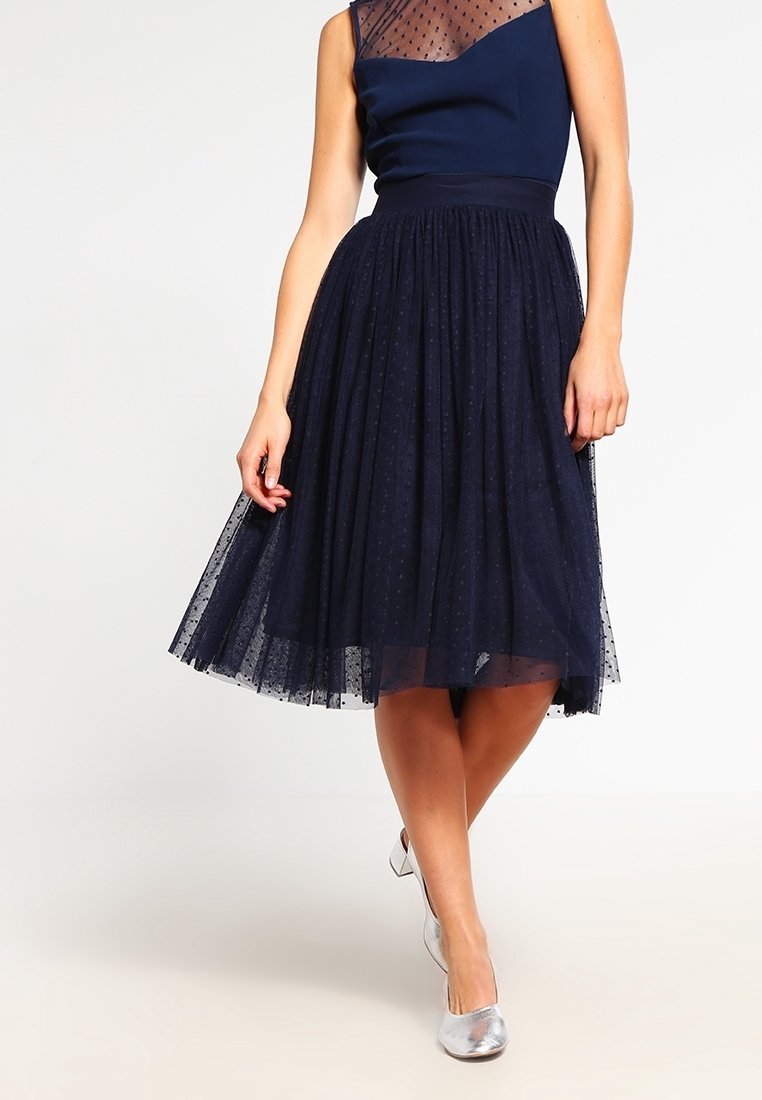 Abito blu navy con un corsetto in chiffon a pois, vita aderente e una gonna in tulle ampia; abbinato a scarpe ballerine argentate.