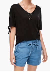 Svart, kortärmad V-ringad skjorta med uppvikta ärmar, kombinerad med blå denimshorts som har en knytbar midja och framfickor.