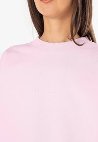 Felpa rosa chiaro con scollo rotondo. Presenta un logo in rilievo sobrio che riporta la scritta "PEGADOR" sul davanti. Tessuto morbido e vestibilità rilassata.