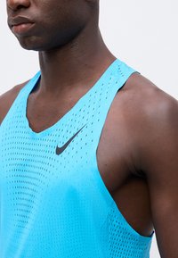 Gros plan d'une personne portant un top de sport sans manches bleu Nike avec de petits trous de ventilation sur un fond clair.