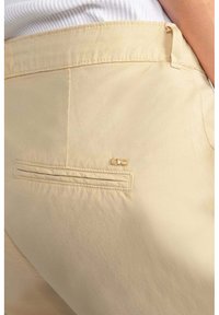 Beige broek van gladde stof met een achterzak met een plooitje en een klein gouden "LTC" logo op de zak.