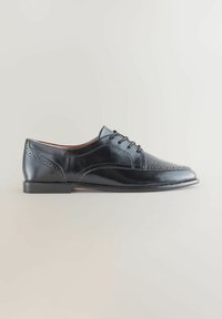 Chaussure habillée Oxford pour homme en cuir noir, avec des détails en brogue et des lacets, montrée de côté sur un fond clair.