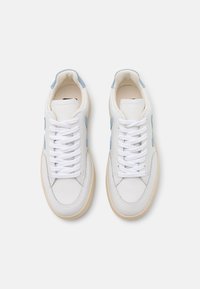 Un paio di sneakers bianche in pelle con accenti in suede blu chiaro, lacci bianchi e suole in gomma beige, viste dall'alto su uno sfondo bianco.