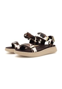 Brown and white cow-print sandals with multiple adjustable straps, a cushioned footbed, and a tan rubber sole featuring textured detailing.