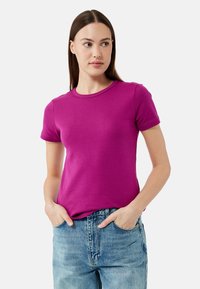 Kurze Ärmel, Rundhals-T-Shirt aus einfarbigem lila Baumwollstoff mit einer taillierten Passform. Kombiniert mit hochgeschnittenen blauen Jeans.
