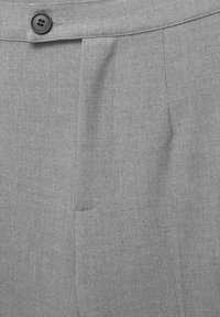 Tissu gris en gros plan d'un pantalon sur mesure avec un bouton noir et une poche latérale visible au niveau de la ceinture.