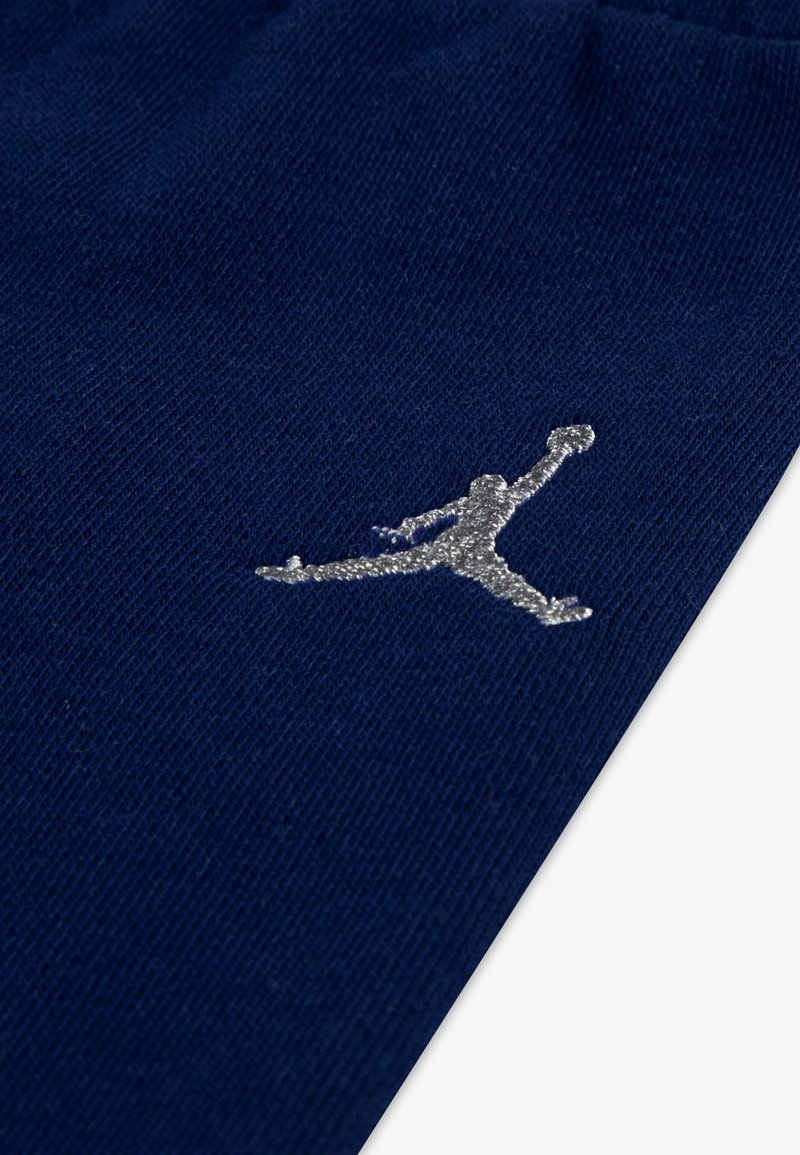 Niebieska tkanina o gładkiej teksturze, z haftowanym w srebrnym kolorze logo Jumpman w dolnym prawym rogu.