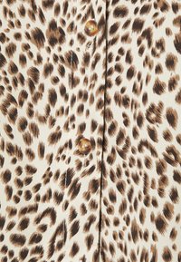 Camisa com padrão de leopardo, apresentando um fundo bege com manchas castanhas escuras e pretas, acentuada com um botão redondo e brilhante.