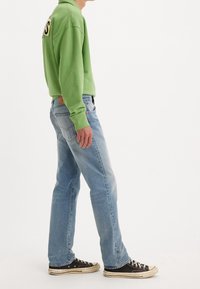 Grön sweatshirt med en logotypapplikation, ljusblå jeans och svarta sneakers med vita sulor. Outfitten har en avslappnad passform och en informell stil.