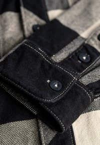 Black and white plaid shirt collar with a contrasting textured fabric. Features black buttons and white stitching accents.