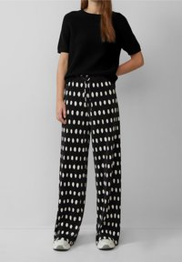 Top negro de manga corta combinado con pantalones sueltos y plisados que presentan un patrón de puntos blancos. El conjunto incluye zapatillas de color claro.