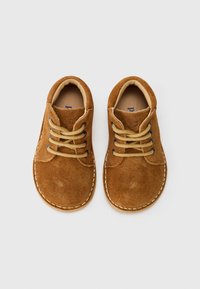Scarpe in suede marrone con lacci beige a contrasto, punta arrotondata e cuciture bianche lungo i bordi. Fodera interna morbida.
