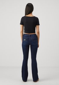 Svart kort t-shirt med korta ärmar kombinerad med mörkblå utsvängda jeans med två bakfickor och logodetalj. Slät tygstruktur.