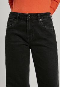 Svarta jeans i denim med åtsittande midja, framfickor och klassisk knappstängning. Slät yta med minimal blekning och raka ben.