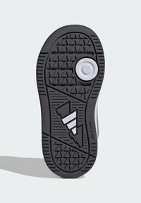Czarna gumowa podeszwa sportowego buta z fakturowanym wzorem bieżnika, okrągłym logo oraz trzema białymi skośnymi paskami.