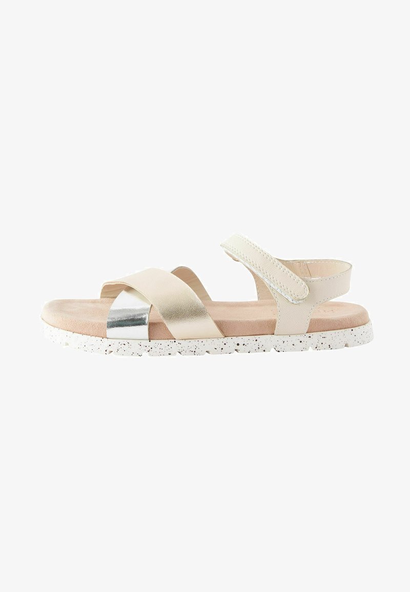 Sandale beige avec design à sangle croisée, accent métallique, sangle ajustable et semelle texturée avec des détails blancs mouchetés.