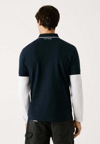 Marineblå polo t-shirt med hvide kraveaccenter, med brandnavnet "PEPE JEANS" på nakken. Materialet ser glat og let ud.