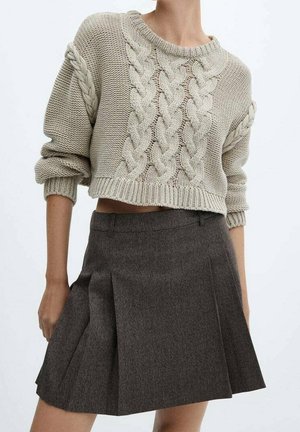 Gruby sweter w splot warkocza w jasnobeżowym kolorze, o krótkim kroju, z wywiniętymi mankietami. Połączony z ciemnoszaro plisowaną mini spódnicą.