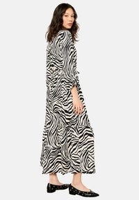 Abito maxi in stampa zebra bianco e nero con maniche lunghe, vita con nastro e orlo arricciato. Abbinato a scarpe piatte nere con accenti argentati.