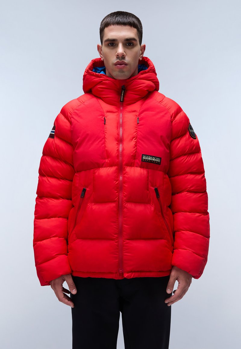 Chaqueta acolchada roja con capucha, bolsillos con cremallera y un parche con el logo. Fabricada con material acolchado de textura suave y un interior azul que contrasta.