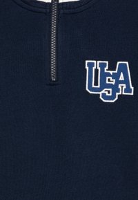 Pullover in pile blu navy con zip a quarto e ricamo "USA" in bianco e azzurro, dotato di una texture liscia e di una robusta dettagli di zip.
