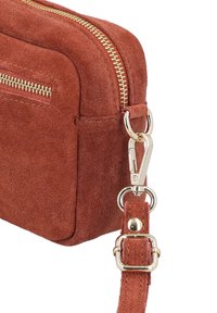 Braune Wildleder-Umhängetasche mit goldenem Reißverschluss, rechteckiger Form, verstellbarem Riemen und Metallbeschlägen. Strukturierte Oberfläche, kompakte Gestaltung.