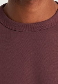 Sudadera de algodón burdeos con cuello redondo acanalado y una textura sutil, con una vista en primer plano de la tela y el escote.