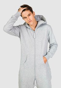 Grijze zip-up onesie van zacht stof, met een capuchon, lange mouwen, twee voorkruiszakken en een logo op de borst.