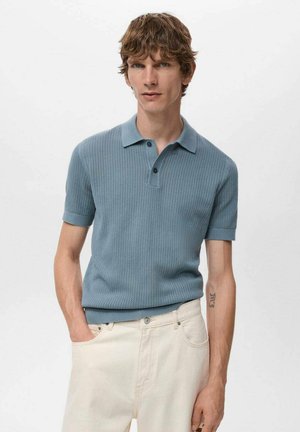 Polo de punto azul con mangas cortas, cuello y tres botones negros. Combinado con pantalones de color claro. Textura suave y diseño ajustado.