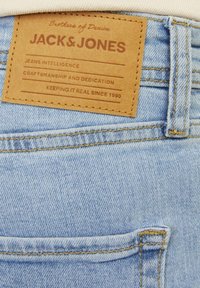Light blue denim jeans pocket with brown leather patch labeled "JACK & JONES" and stitched yellow seams.
