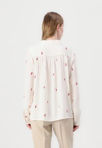 Light-colored blouse with back pleat, long sleeves, and red embroidered accents. Smooth fabric with a collar and button cuffs.