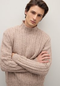 Maglione beige lavorato a maglia con colletto alto, maniche lunghe e motivi testurizzati. Materiale morbido con un aspetto spesso e accogliente.