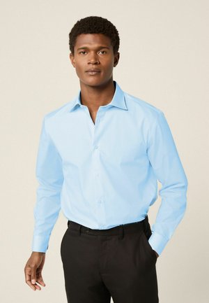 Light blue button-up shirt with a pointed collar and long sleeves, paired with black trousers. Smooth fabric with a classic fit.