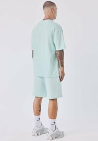 T-shirt en coton vert menthe à manches courtes et short assorti. Coupe ample, design col rond, associé à des chaussettes blanches à la cheville et des baskets grises.